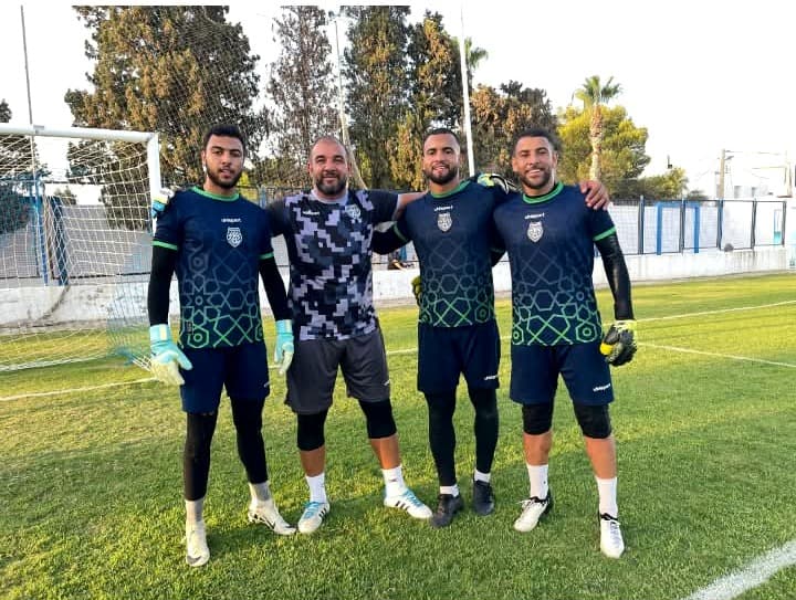 Raouf Rattouli entouré de trois gardiens de but qu'il entraîne, posant ensemble sur le terrain d'entraînement.